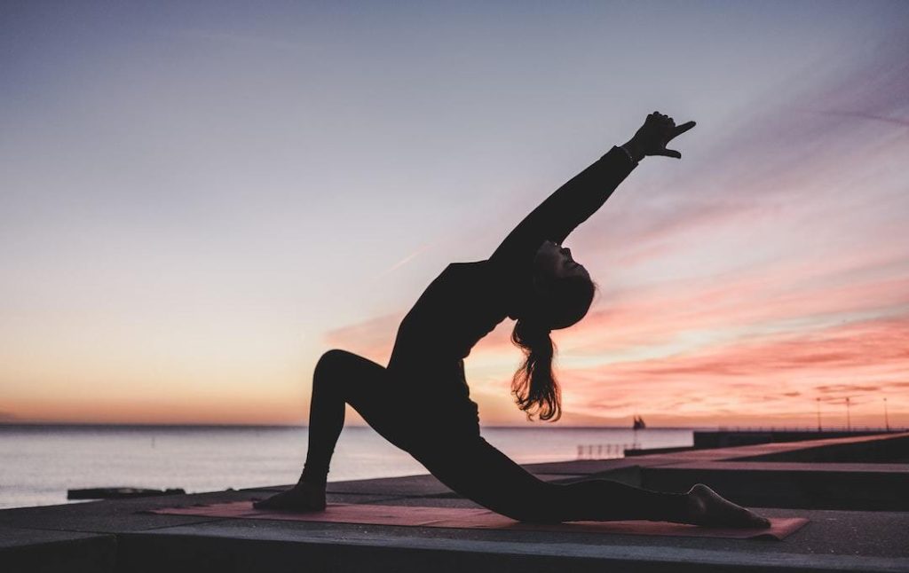 Yoga vs pilates - Woman doing a yoga pose on her mat by the water