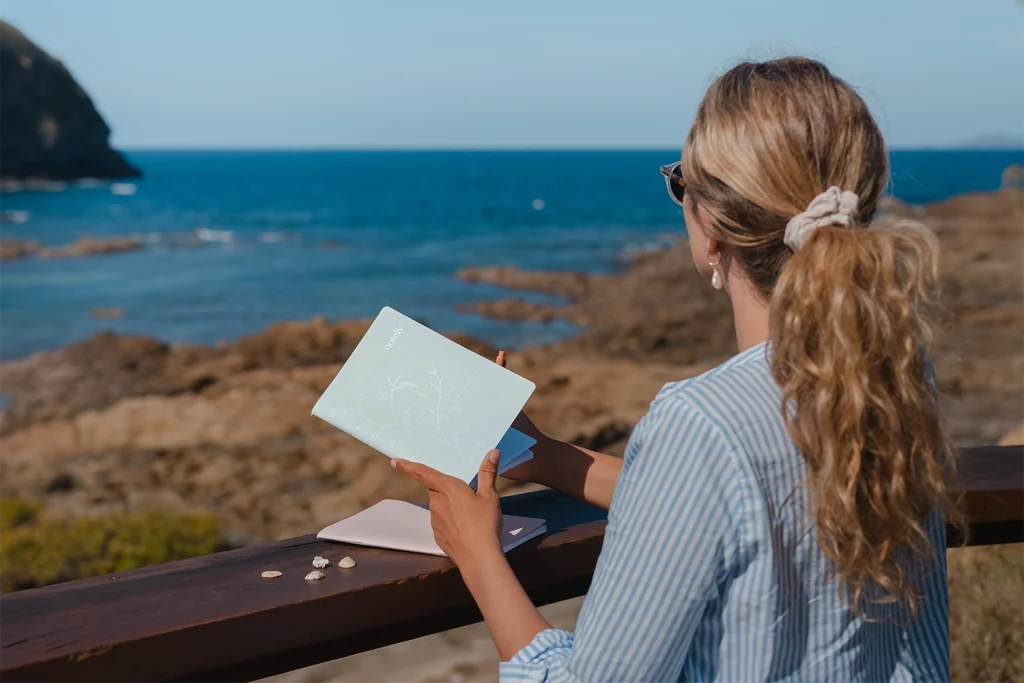 Digital detox and woman with her notebooks by the ocean